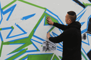 Los Angeles artist Tommii Lim applies masking tape to the side of the ARTery in Atascadero. The drawing below his left hand show what the mural will look like when it is completed. Photo by Heather Young