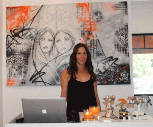 Farron Day stands in front of a painting she commissioned Adam Welch to paint for the store. Photo by Heather Young