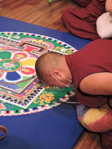 Colored sand is gently tapped out of metal funnels onto the mat. Photo by Skye Ravy.