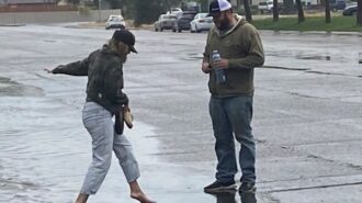 In order to keep her shoes try, a young woman wades through standing water barefoot.