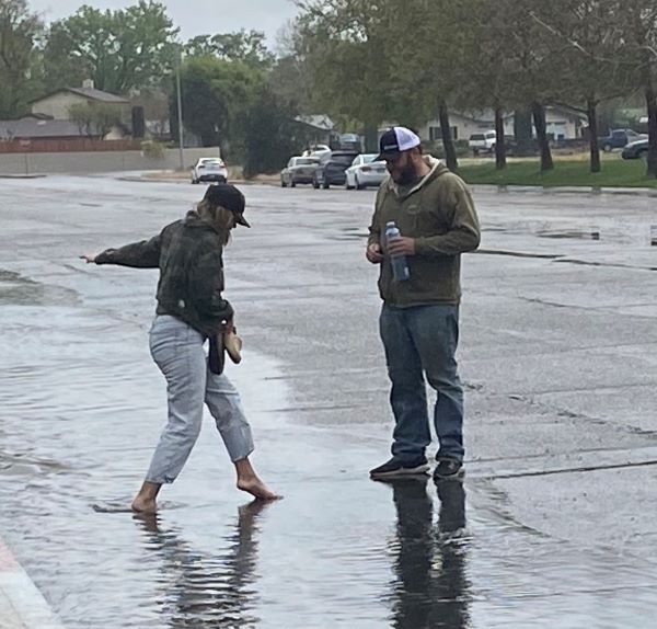 In order to keep her shoes try, a young woman wades through standing water barefoot.